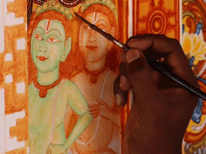 a close up shot of an artist's hand as they paint a Kerala Mural Painting.